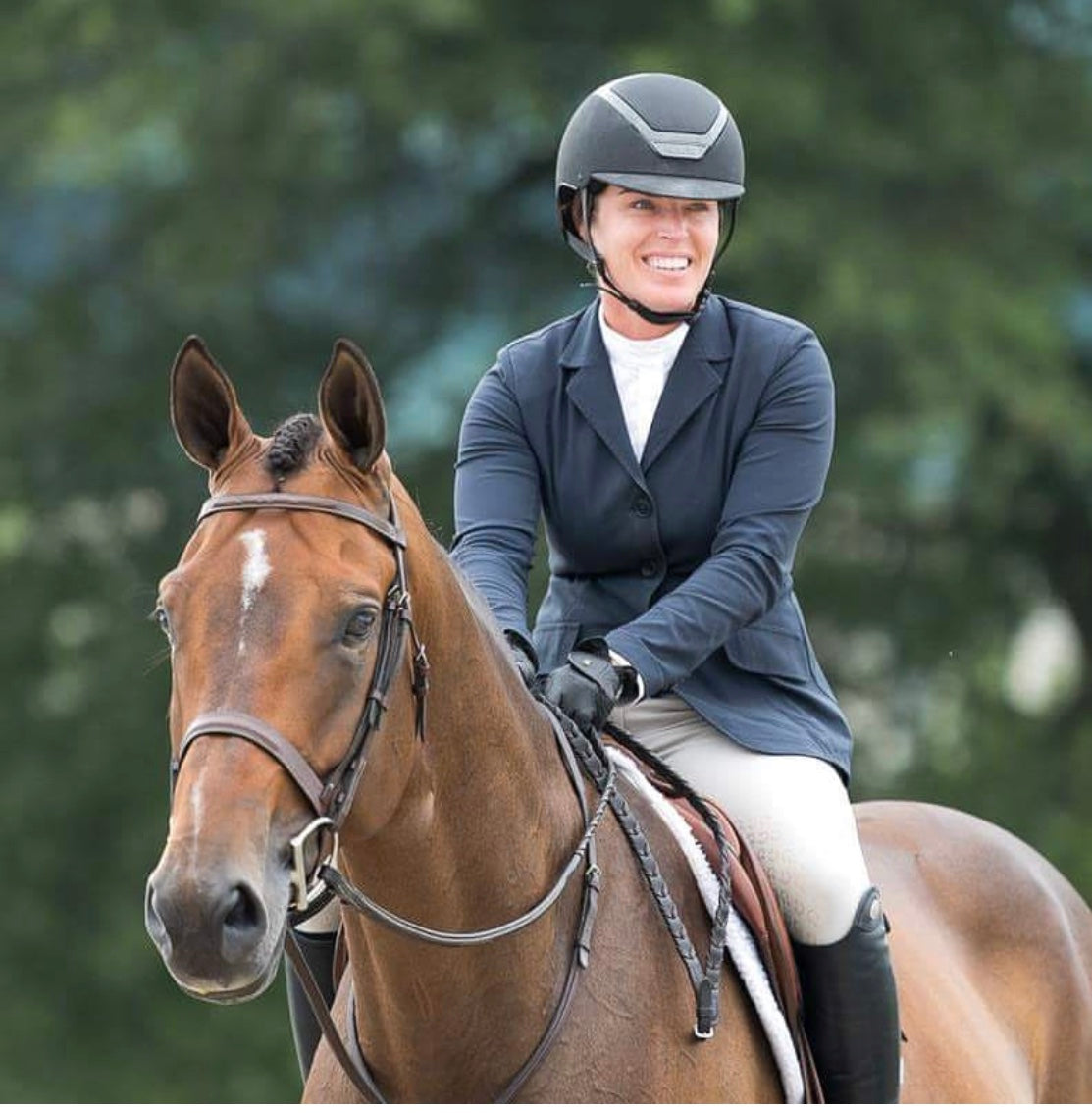 Equestrian woman sitting on brown horse smiling wearing a KASK helmet and hunter show clothes